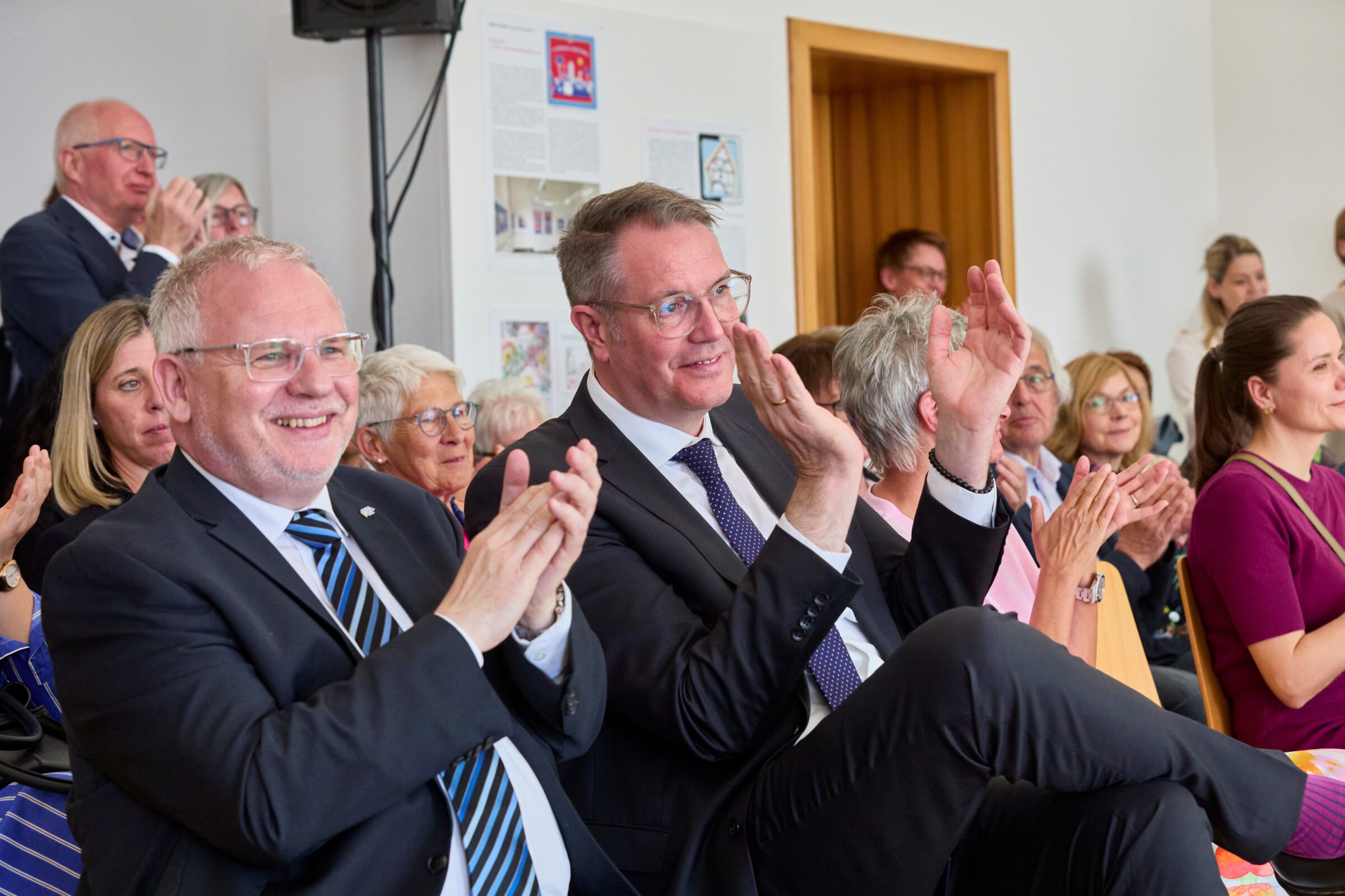 Ministerpräsident von Rheinland-Pfalz (Alexander Schweitzer) und Vorsitzender des Bezirkstags Pfalz (Hans-Ulrich Ihlenfeld) Applaudieren lächelnd im Zuschauerraum einer Rede