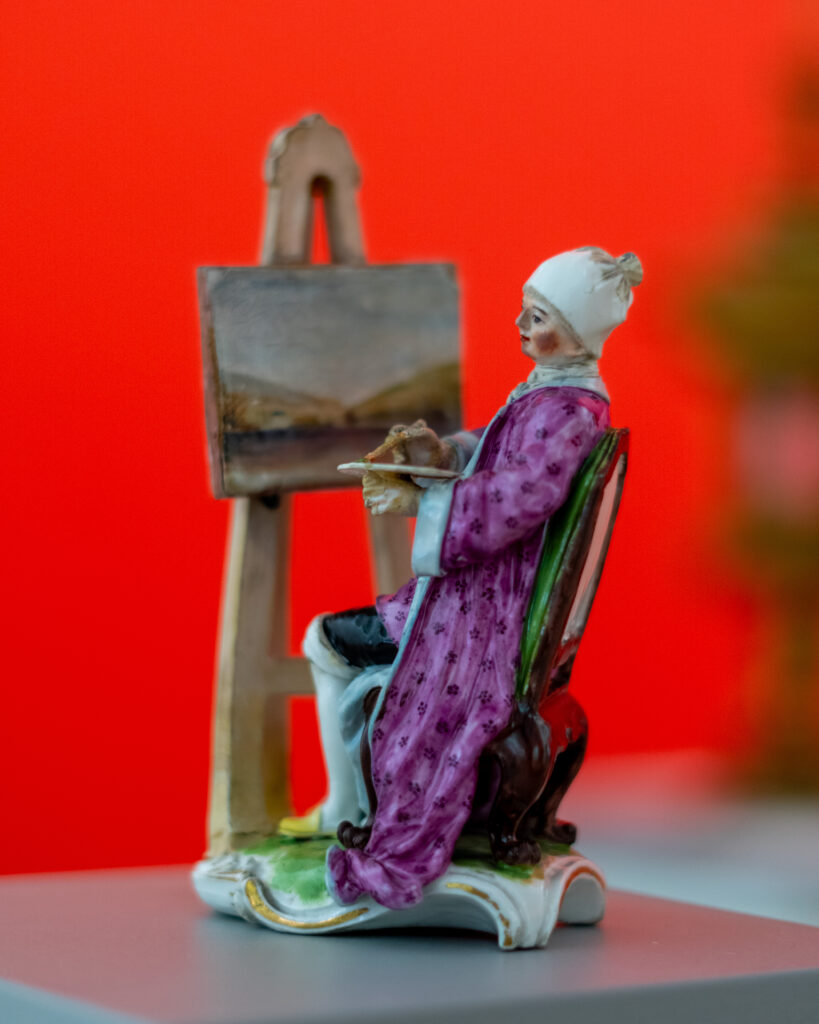 Figur einer zeichnenden Dame vor rotem Hintergrund im mpk