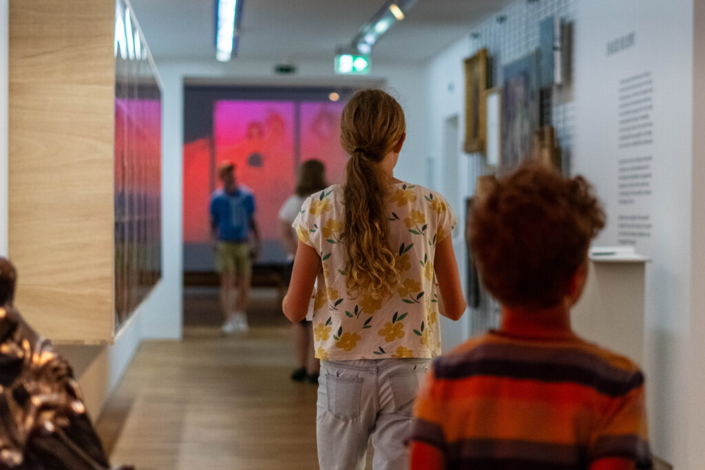 Mädchen und Junge laufen einen mit Kunst gefüllten Korridor entlang