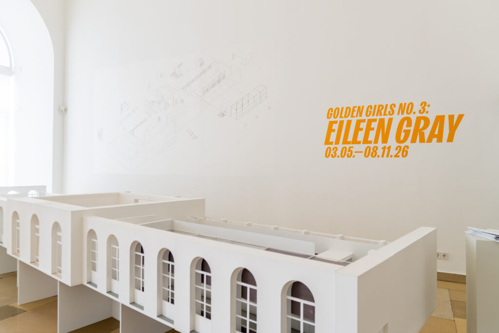 Architekturmodell der Ausstellung „Golden Girls No. 3: Eileen Gray“ im mpk Museum Pfalzgalerie Kaiserslautern vor weißer Museumswand mit orangefarbenem Ausstellungstitel als eindrucksvolle Präsentation moderner Architektur- und Designgeschichte.